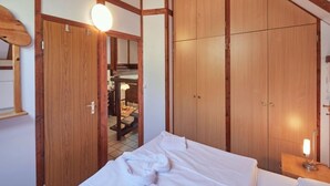 Quarto de hotel com cama, guarda-roupa de madeira e uma pequena mesa com abajur.