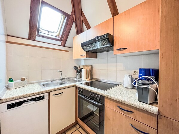 A compact kitchen with a dishwasher, oven, and a built-in microwave. There is a window above the sink, and wooden cabinets are present.