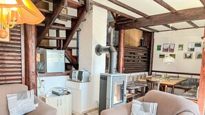 Interior acolhedor de uma cabana, com uma escada de madeira, cozinha com fogão e assentos com almofadas estampadas.