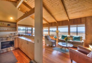 Amplia sala de estar con cocina, ventanas grandes y vista a la playa.