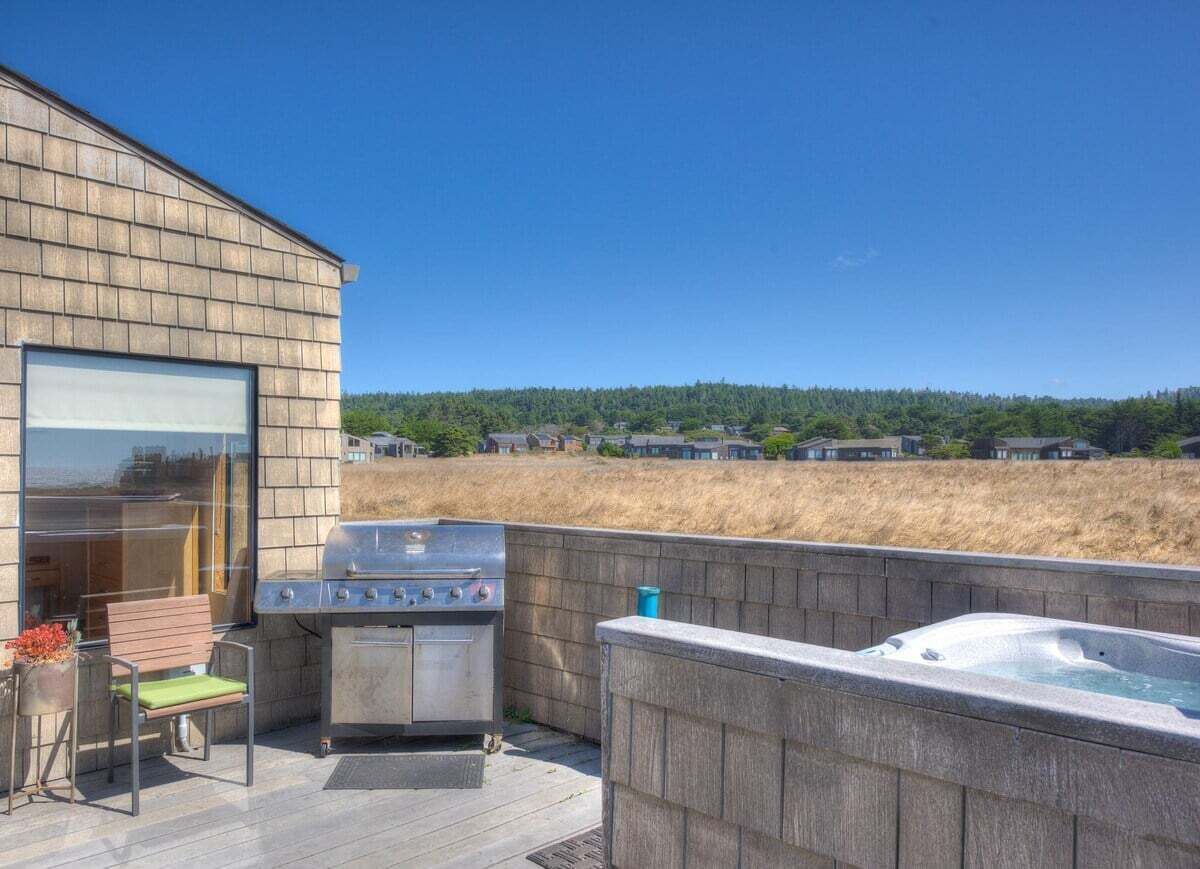 A deck with a barbecue grill, a hot tub, and a seating area with a view of a forested hill.