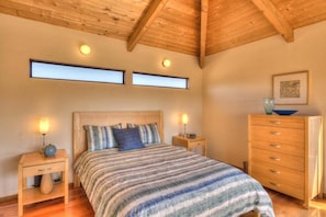 A bedroom with a wooden ceiling, a bed with striped bedding, two bedside tables with lamps, a wooden dresser, and a framed picture on the wall.