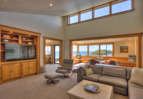 A spacious living area with a large flat-screen TV, comfortable seating, and a view of the ocean.