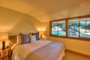 A bedroom with a large bed, two bedside lamps, a window with a view of trees, and a wooden headboard. - Sculpture Point - Sea Ranch Whitewater Vista Lodge (Sea Ranch)