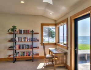 Une pièce avec une bibliothèque en bois, un bureau et une vue sur l’océan grâce à de grandes fenêtres.