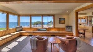 Quarto com uma grande janela com vista para o mar, um espaço de estar com bancos embutidos e uma pequena mesa.