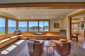 A room with a large window overlooking the sea, a built-in bench seating area, and a small table. - Sculpture Point - Sea Ranch Whitewater Vista Lodge (Sea Ranch)