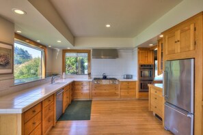 A modern kitchen with wooden cabinets, stainless steel appliances, and a large window offering a view of greenery. - Sculpture Point - Sea Ranch Whitewater Vista Lodge (Sea Ranch)