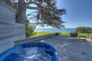 A hot tub on a wooden deck with a view of the ocean.