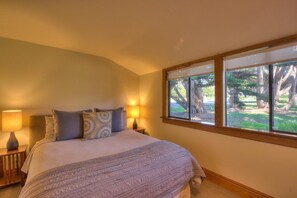 Een slaapkamer met een groot bed, twee bedlampen en een raam met uitzicht op bomen.