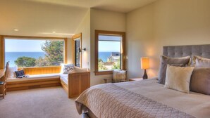 Um quarto com uma cama grande, um assento junto à janela e vista para o mar.