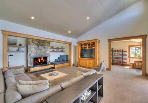 A spacious living room with a stone fireplace, comfortable seating, a flat-screen TV, and a bookshelf.