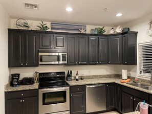 A kitchen with dark cabinets, stainless steel appliances, granite countertops, and decorative wall art.