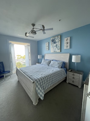A bedroom with a bed, two bedside tables, a ceiling fan, and artwork on the wall.
