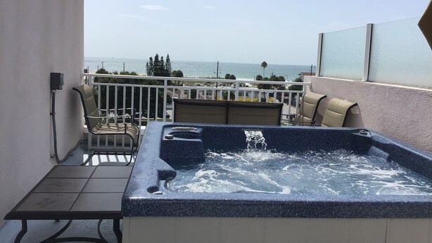 A balcony with a hot tub, seating area, and a view of the ocean.