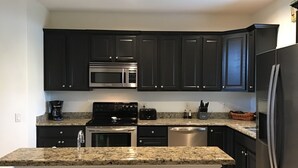 A modern kitchen with dark cabinetry, a granite countertop, stainless steel appliances, and a built-in island.