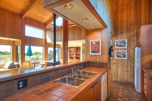 A modern kitchen with a large island, built-in shelves, and a view of the outdoors. - Kenber House – Don Jacobs Coastal Near Shell Beach (Sea Ranch)