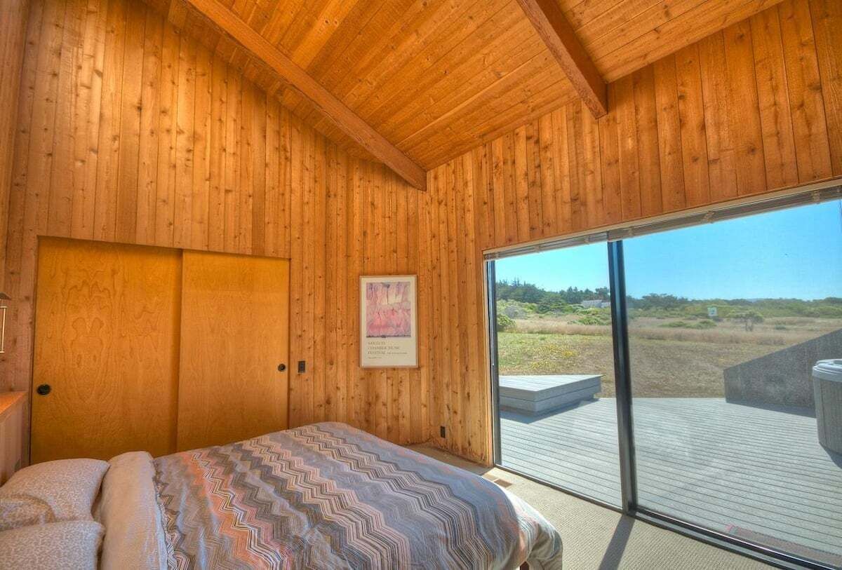 Un dormitorio con paneles de madera, una cama, un ventanal y vistas al exterior.