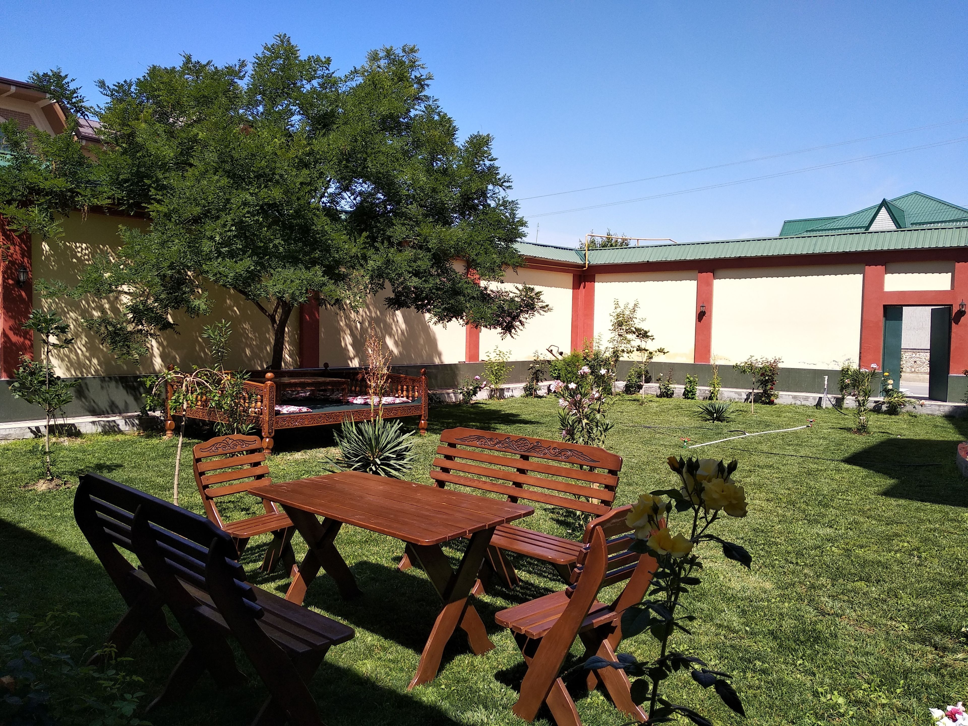 An outdoor seating area with wooden benches and tables, surrounded by well-maintained grass and small plants.