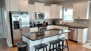 A modern kitchen with white cabinets, stainless steel appliances, a central island with stools, and a wooden floor.