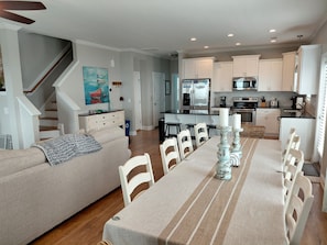 A modern kitchen with white cabinets, a dining table with chairs, and a staircase leading to another level.
