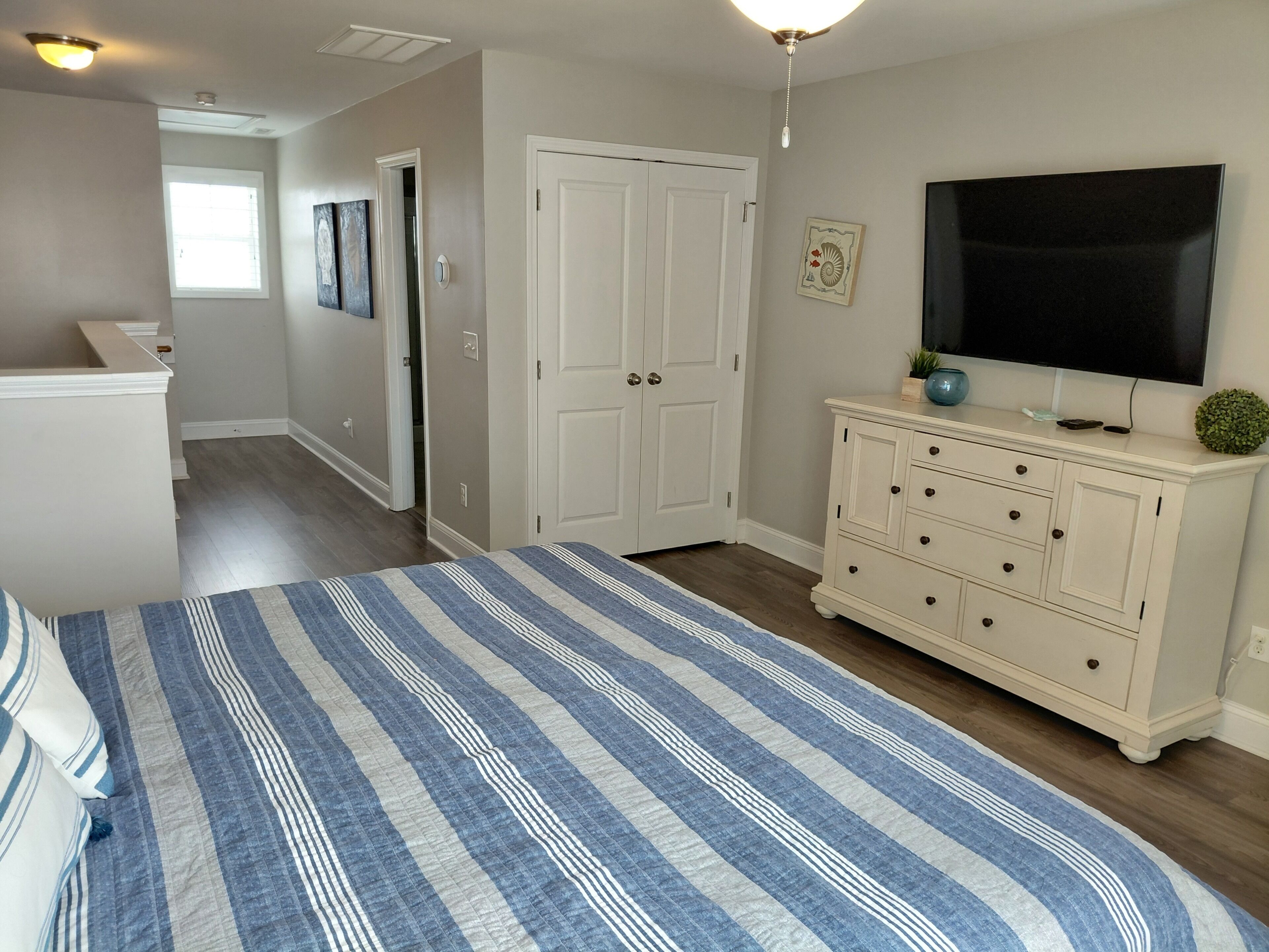 A bedroom with a bed, dresser, television, and a door leading to another room.