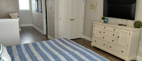A bedroom with a bed, dresser, television, and a door leading to another room.