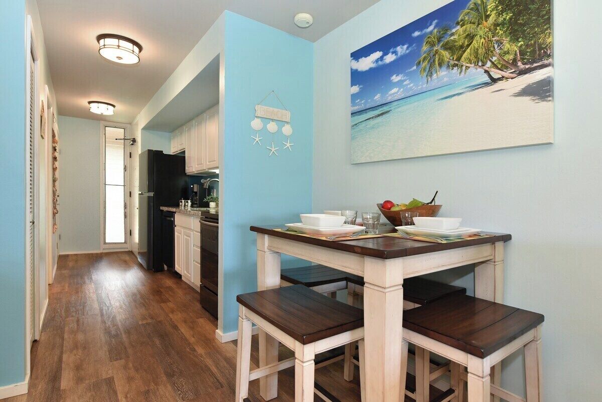 A kitchen with wooden flooring, a dining table with benches, and a wall-mounted light fixture.