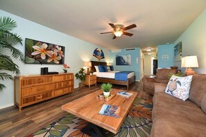 A room with a bed, a sofa, a coffee table, a TV, and a ceiling fan.