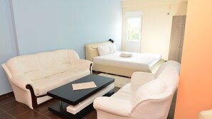 A hotel room with a bed, two white sofas, a black coffee table, and a window with a view of greenery.