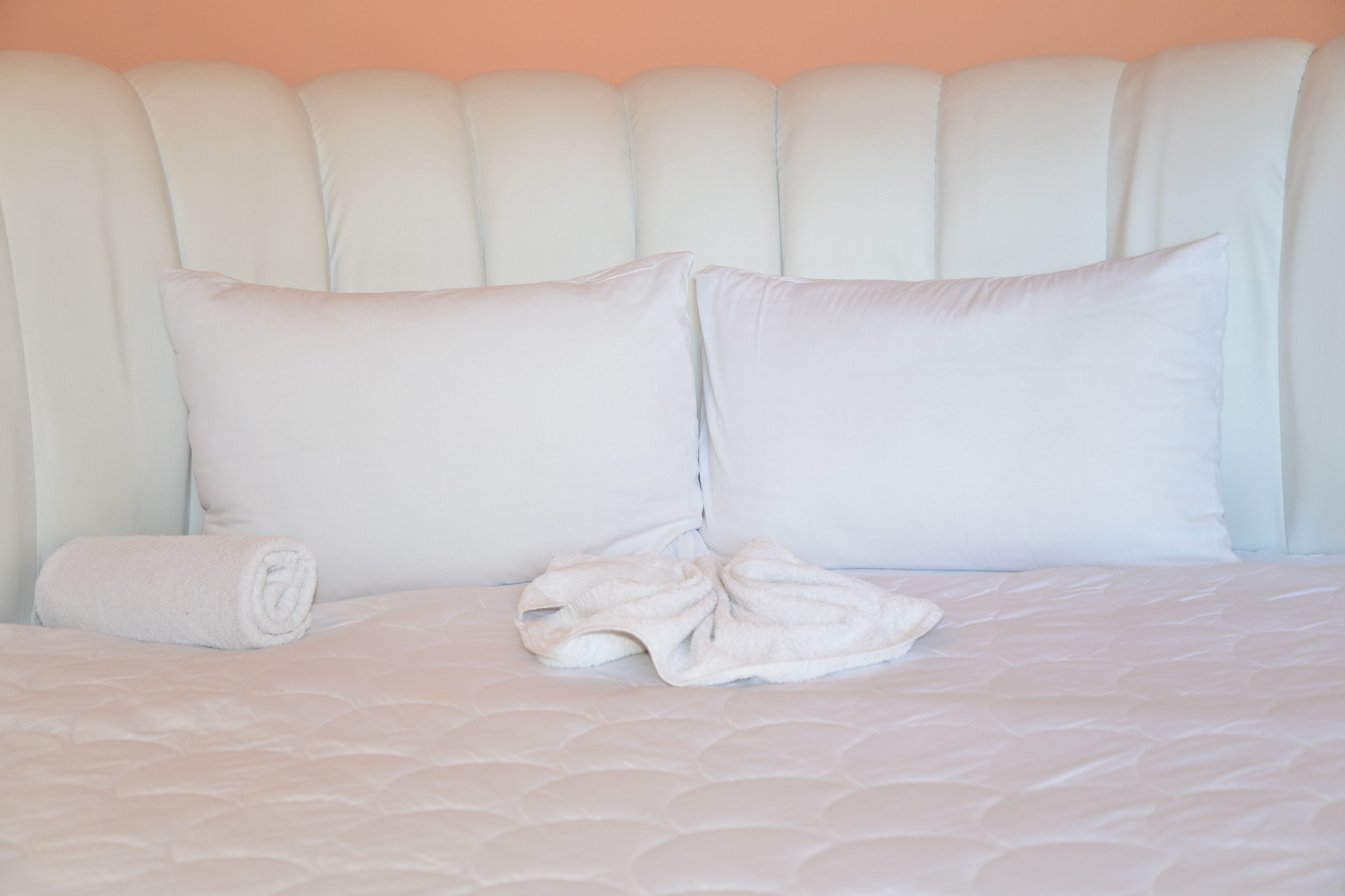 A neatly made bed with a rolled towel and a robe on it.
