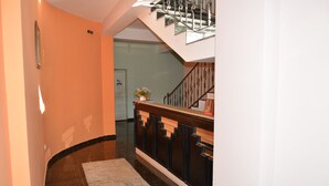 A hallway with a marble floor, a wooden railing, and a staircase with a metal railing.
