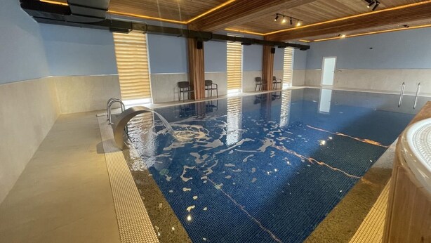 An indoor swimming pool with a wooden ceiling and walls, clear water, and a tiled floor.