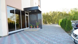 A modern building with a glass entrance, potted plants, and a paved driveway.