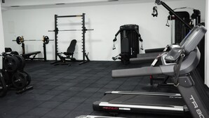 A gym with a treadmill, weight bench, squat rack, and various weights.