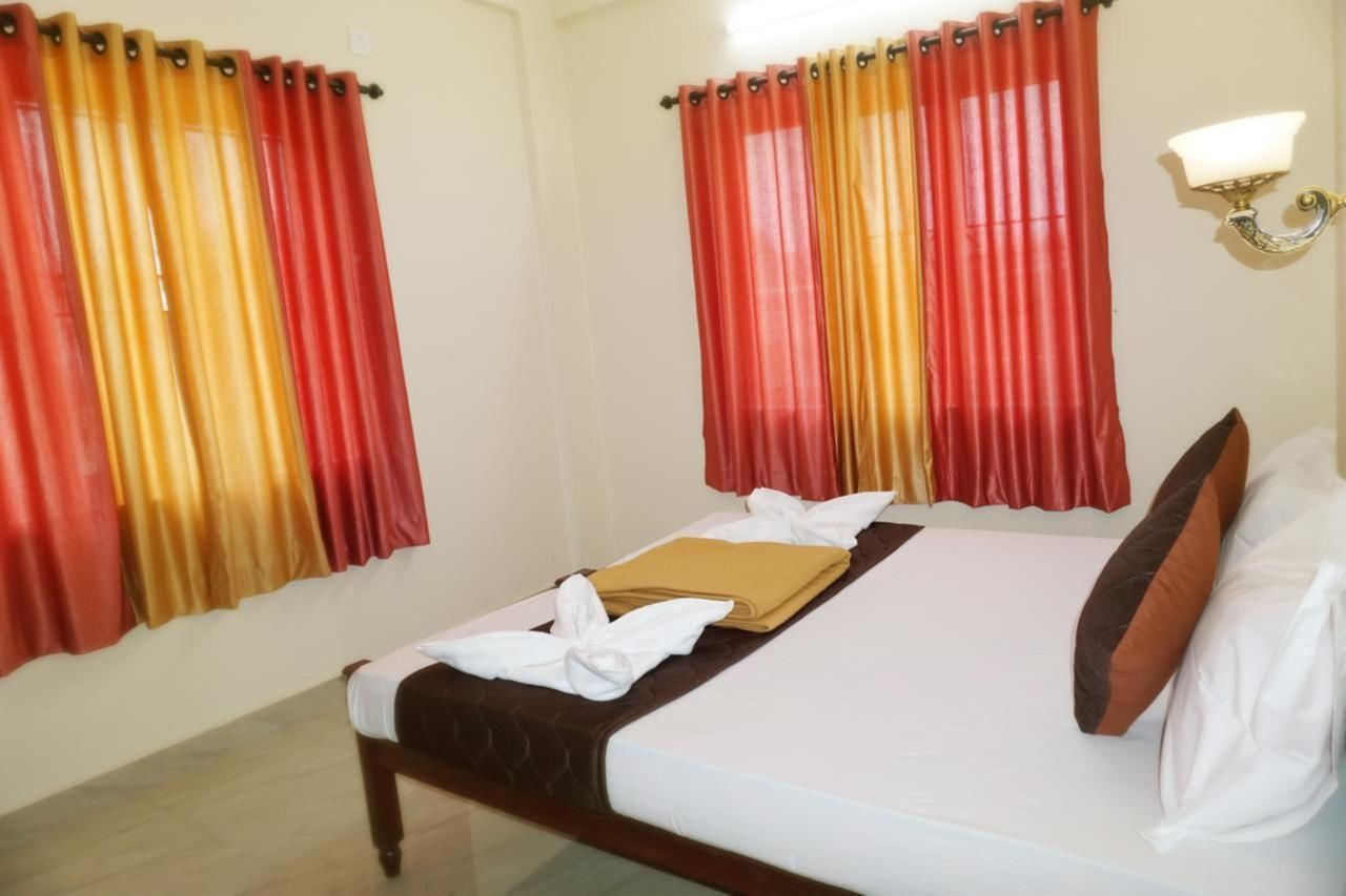 A hotel room with a bed, curtains, a bedside table, and a wall-mounted light fixture.