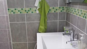 A bathroom with a white sink, grey tiles, a green towel, and a small green plant. - SUBLIME F2 ANY COMFORT (Les Saintes)