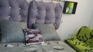 A bedroom with a bed featuring a grey bedspread with a nature-inspired design, two grey pillows, and a decorative pillow with a floral pattern. - SUBLIME F2 ANY COMFORT (Les Saintes)