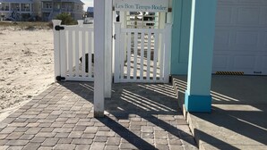 Una entrada frente a la playa, con un portón blanco, un letrero que dice "Chalet Laissez Les Bon Temps Rouler" y un camino pavimentado que lleva a un edificio.