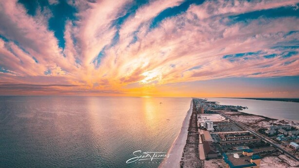 Vista aérea de una zona costera con edificios y una playa durante el atardecer.