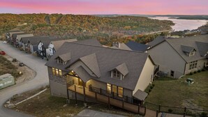 A residential area with houses featuring gabled roofs and large windows, surrounded by autumn foliage and a body of water in the background. - Luxe Lodge: Gaming Paradise W/ Breathtaking Lake Views, Indoor Pool Close to SDC (Branson)