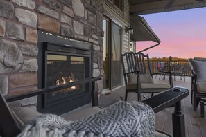 A stone fireplace with a fire, outdoor seating with chairs and a table, and a view of the sky.