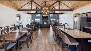 A spacious kitchen with a central island, wooden beams on the ceiling, and a stone fireplace. - Luxe Lodge: Gaming Paradise W/ Breathtaking Lake Views, Indoor Pool Close to SDC (Branson)