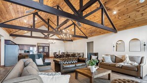 A spacious living area with a high wooden ceiling, leather sofas, a coffee table, and a dining area in the background. - Luxe Lodge: Gaming Paradise W/ Breathtaking Lake Views, Indoor Pool Close to SDC (Branson)