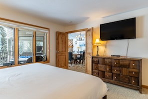 A bedroom with a large bed, a wooden dresser, a flat-screen TV, and a sliding glass door leading to a balcony.