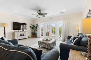 A living room with a ceiling fan, a TV, a sofa, a coffee table, and a view through the glass doors.
