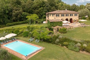 A large house with a swimming pool, surrounded by lush greenery and a well-maintained lawn.