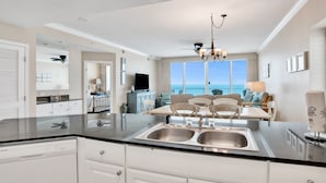 A modern kitchen with a central island, stainless steel sinks, and a dining area with a view of the ocean. - San Carlos 1009 | Beautiful, oversized, beach front, walk to Gulf Shores favorites! (Gulf Shores)