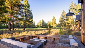 Une terrasse extérieure aménagée avec des meubles en osier et un foyer, entourée d’arbres et d’un champ d’herbe.