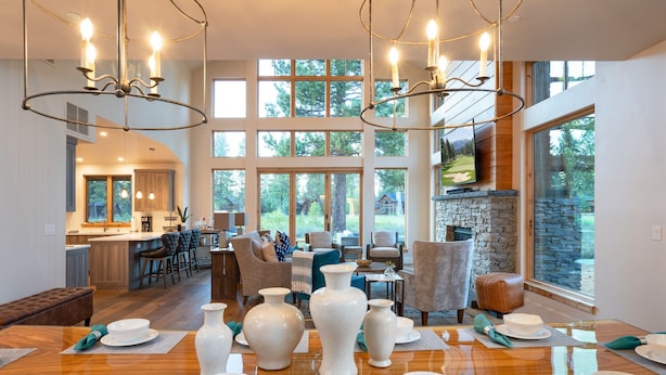 Un vaste espace dédié à la salle à manger, avec une table en bois dressée pour le repas, entourée de sièges confortables. De grandes fenêtres laissent entrer la lumière naturelle et offrent une vue sur l’extérieur.